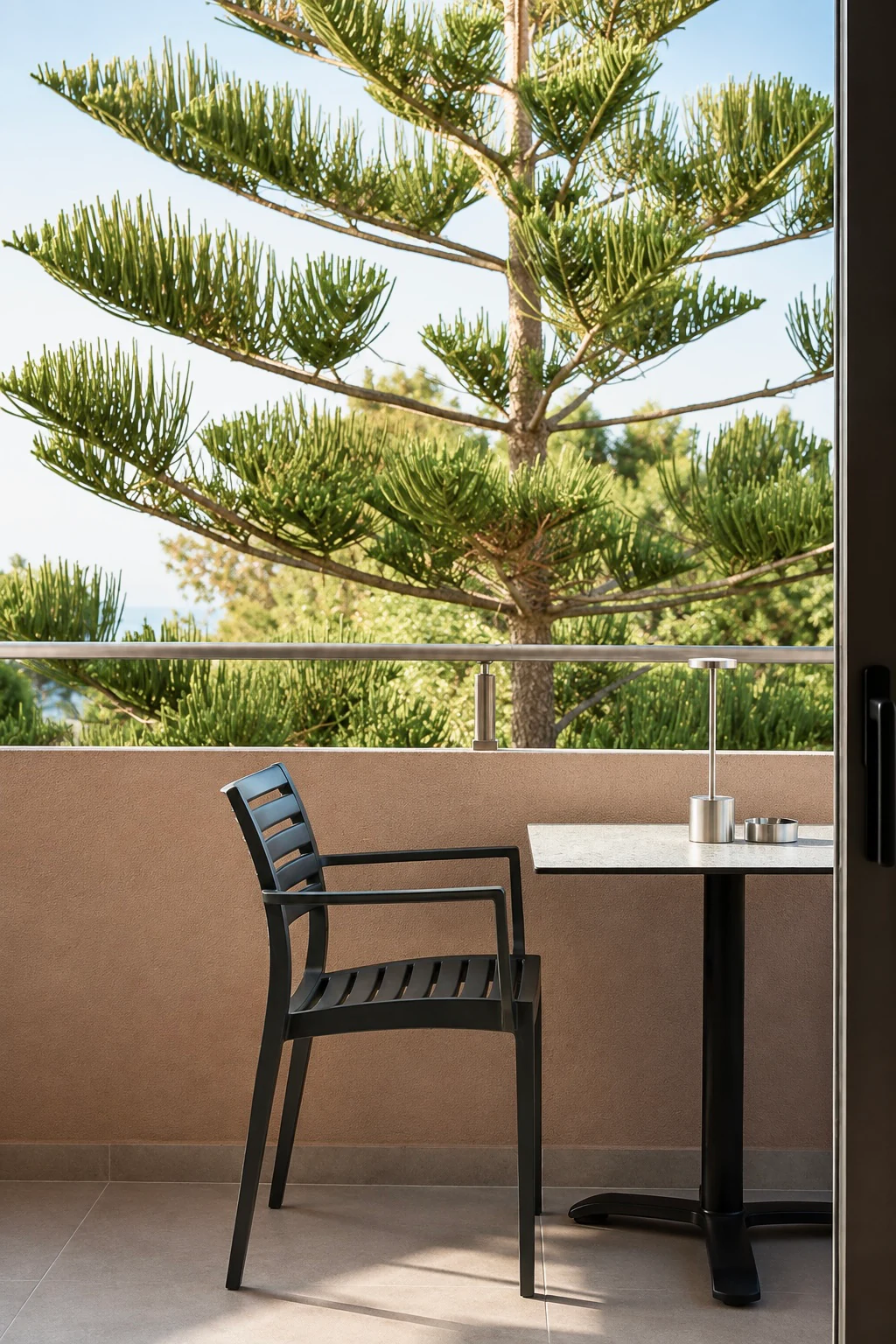 Sunlit balcony with a chair, table and view of the trees at Eos Mare